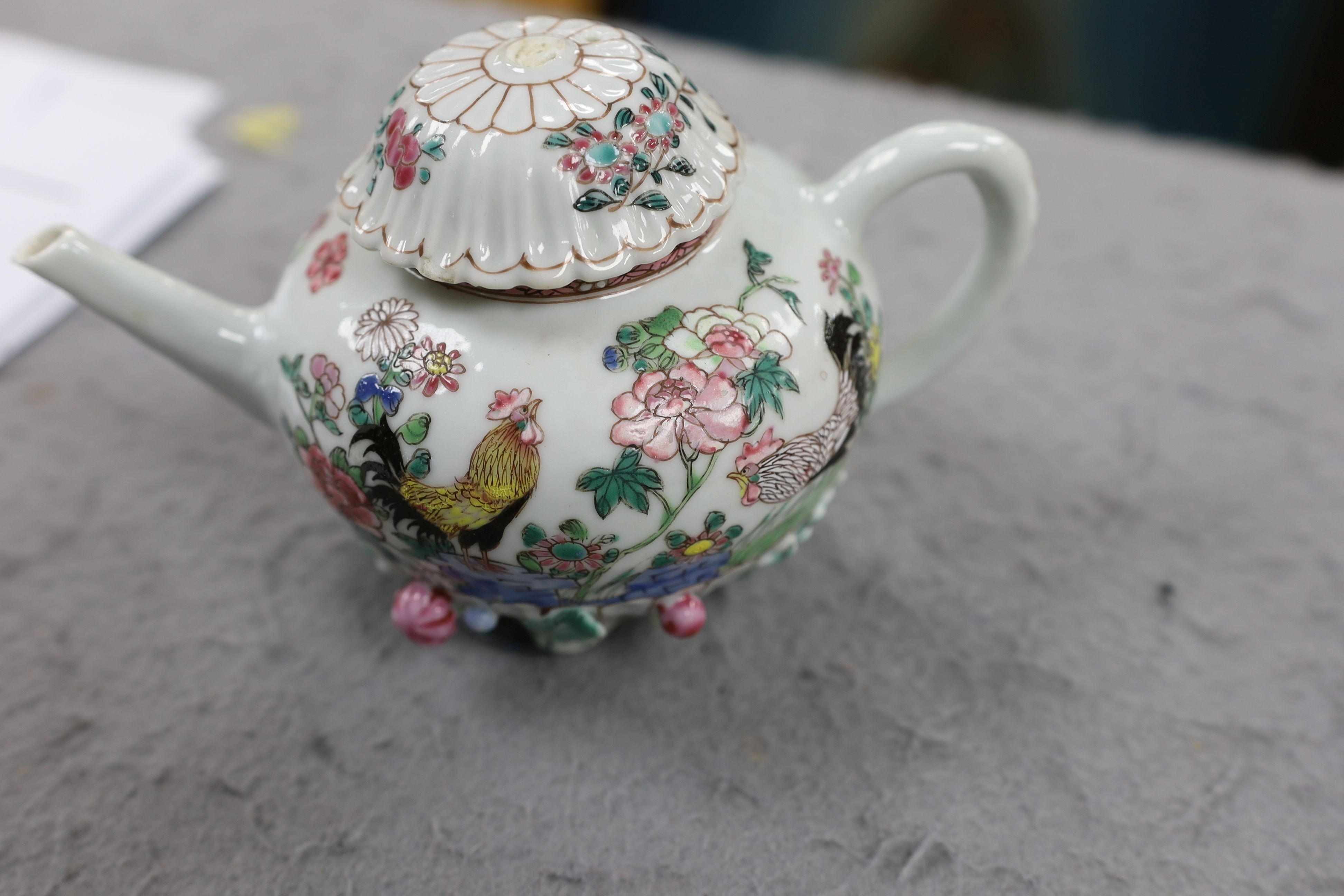 A Chinese famille rose chrysanthemum moulded teapot, early Qianlong period, painted with a cockerel amongst flowers, on a cage work base, 10 cms high